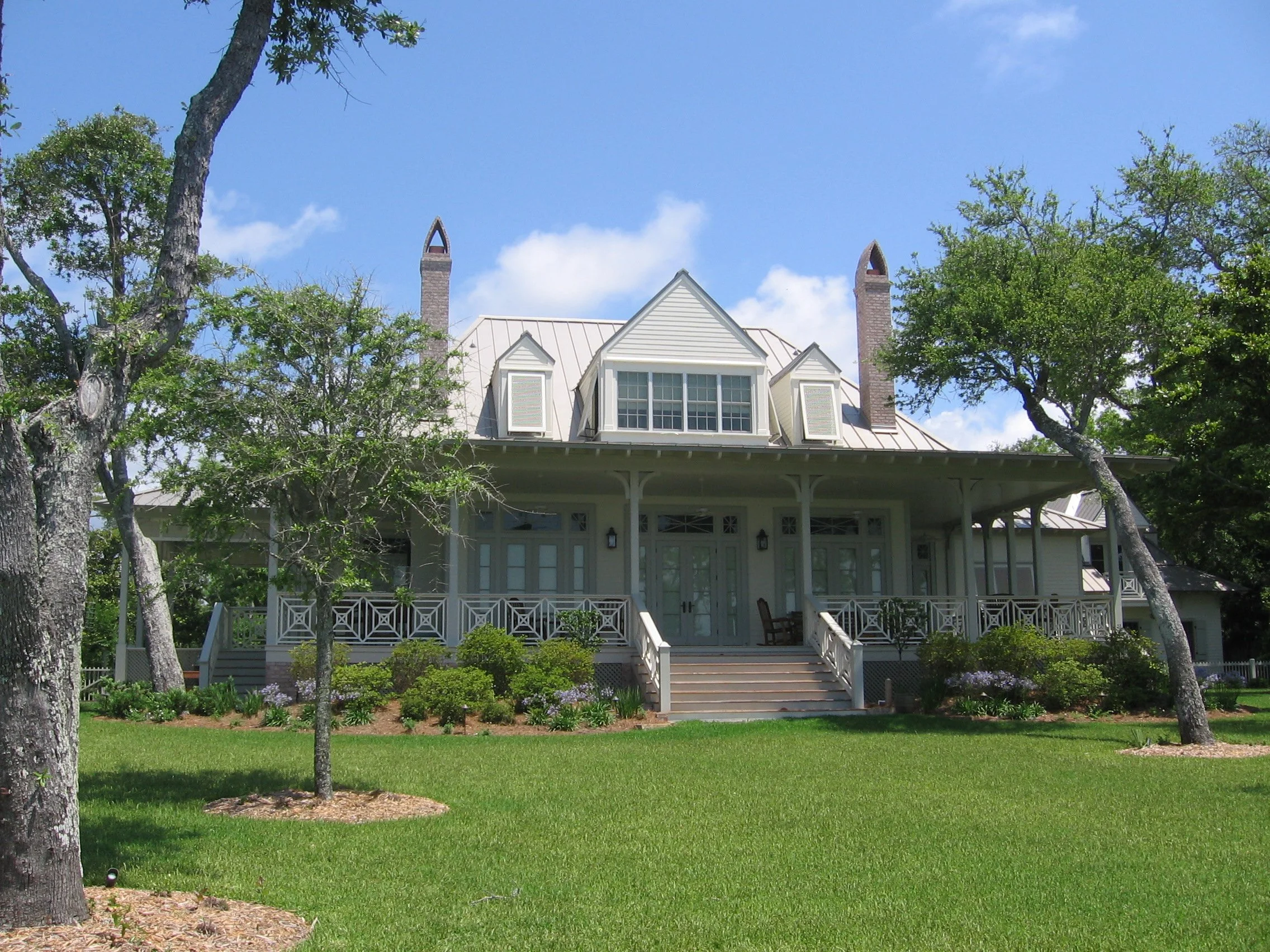 A large white house with a porch, trees in front, and a well-maintained lawn under a partly cloudy sky.
