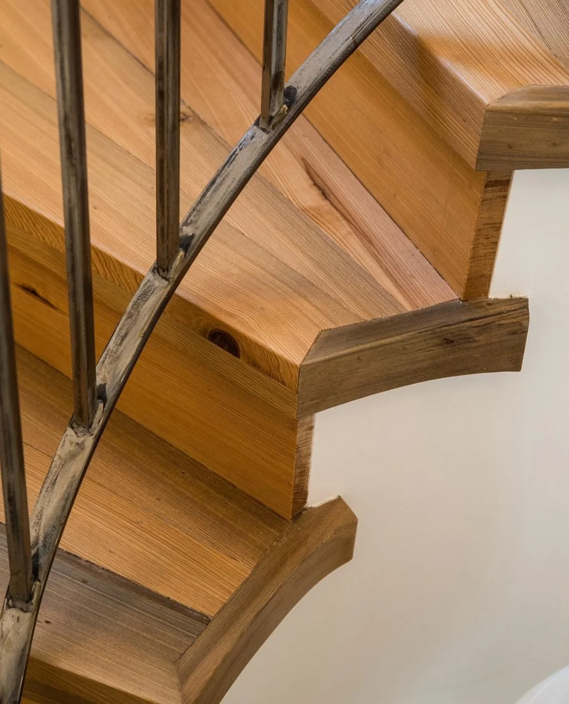 Close-up image of a wooden staircase with metal railing, showing the curved edges and wood grain.
