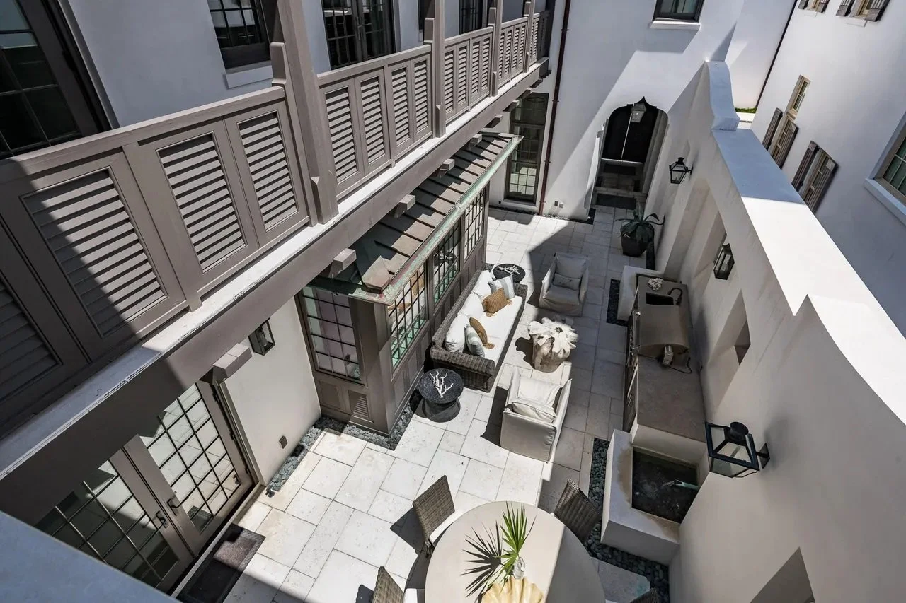 An aerial view of a modern outdoor courtyard with seating, a small fountain, and decorative elements, surrounded by white walls and windows.