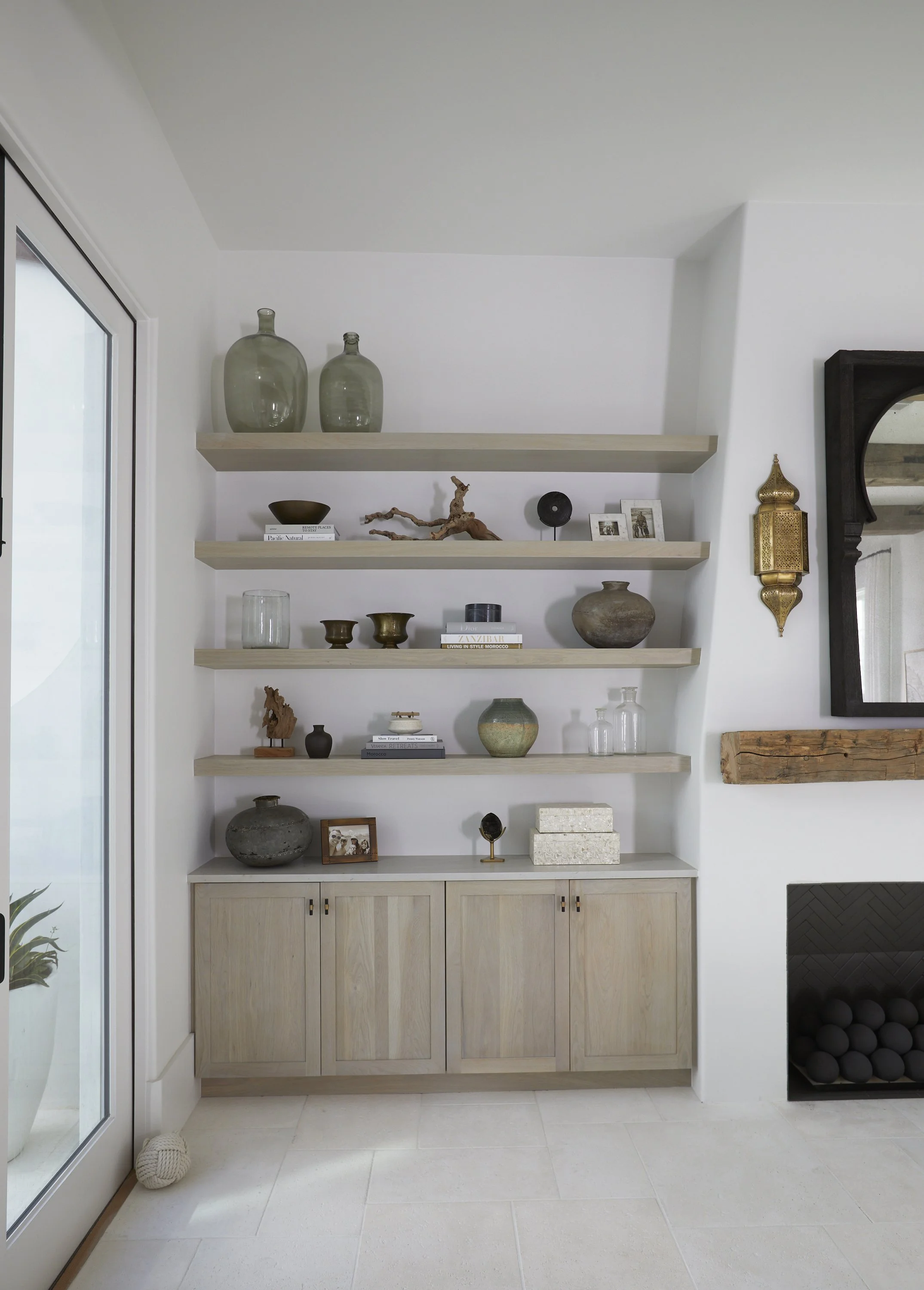 A built-in wooden cabinet with multiple shelves displaying decorative objects, vases, small sculptures, framed photos, and books in a modern, minimalist living room.